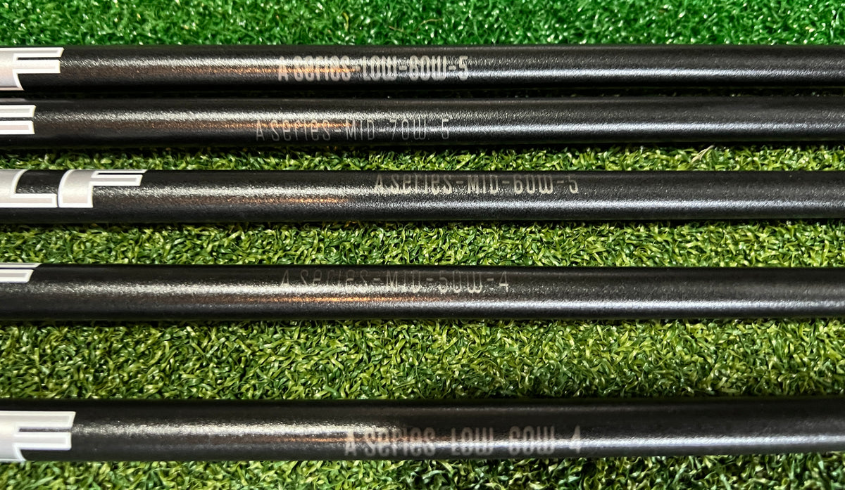 Five black LA GOLF A SERIES shafts with white bands and silver tips laid horizontally on green artificial turf. The shafts are printed with model names including A SERIES LOW SOUL 5 and A SERIES MID SOUL 5.