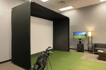 Golf simulator setup in a room with a screen displaying a golf course.
